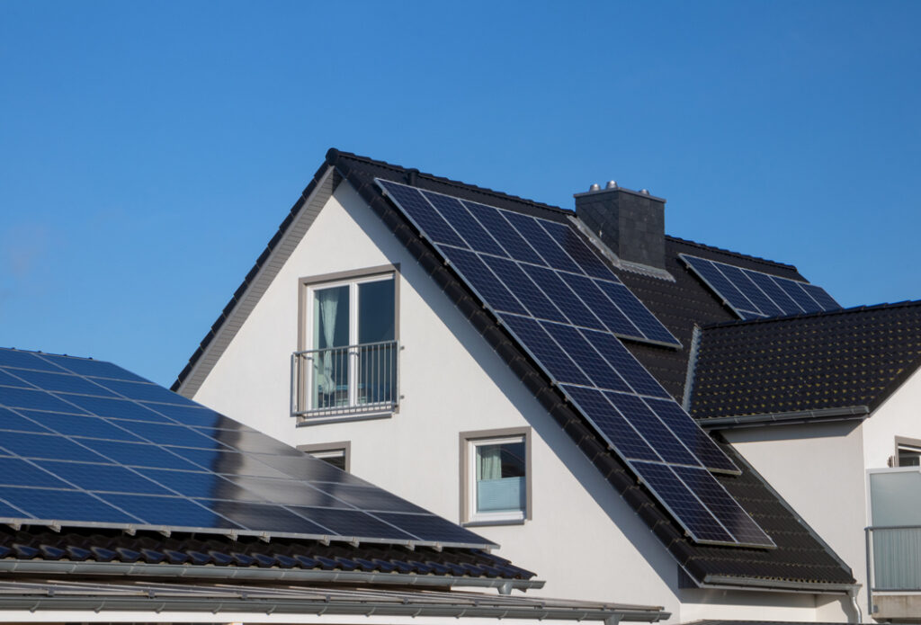 Weiße Häuser mit Solarpaneelen auf den Dächern, blauem Himmel im Hintergrund.