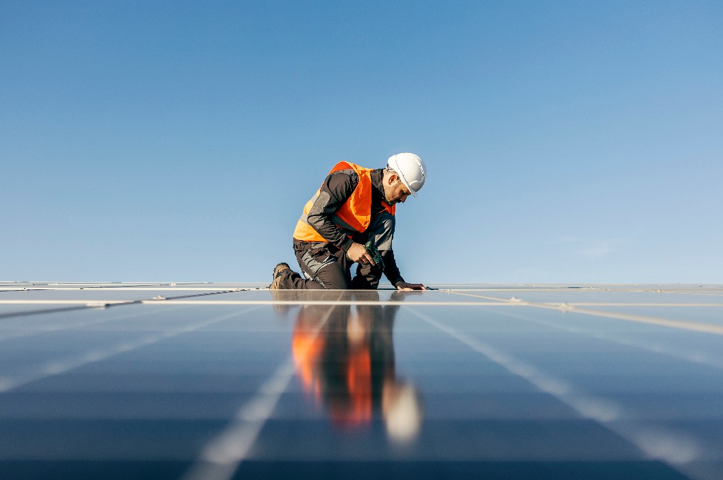 Arbeiter kniet und stellt ein Solarpanel auf.